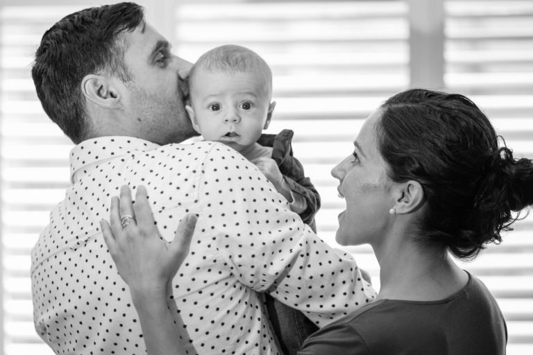 Black and white photograph of a father kissing his baby's head while the mother smiles up at them