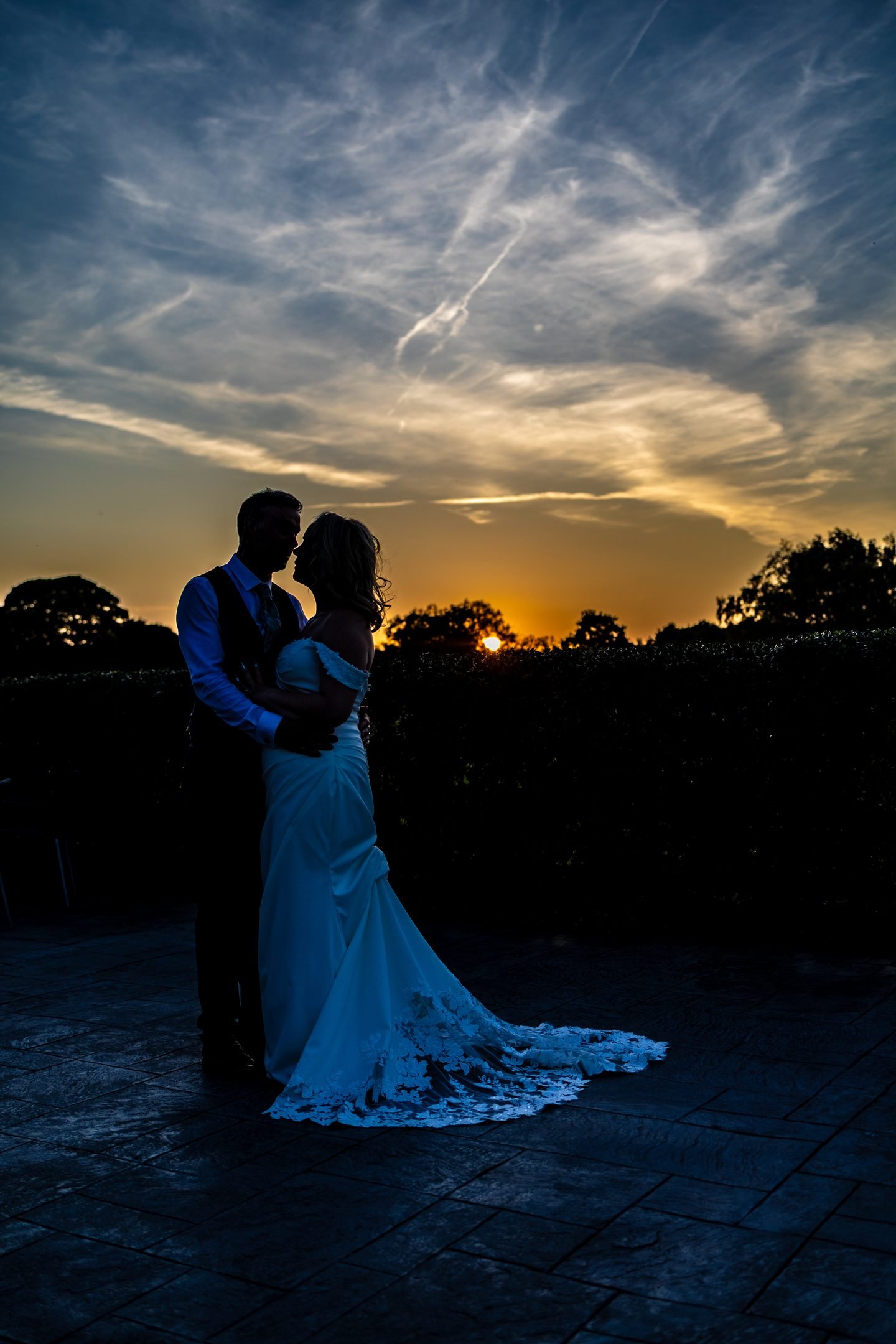 Bride and groom embracing in silhouette against a dramatic blue hour sky