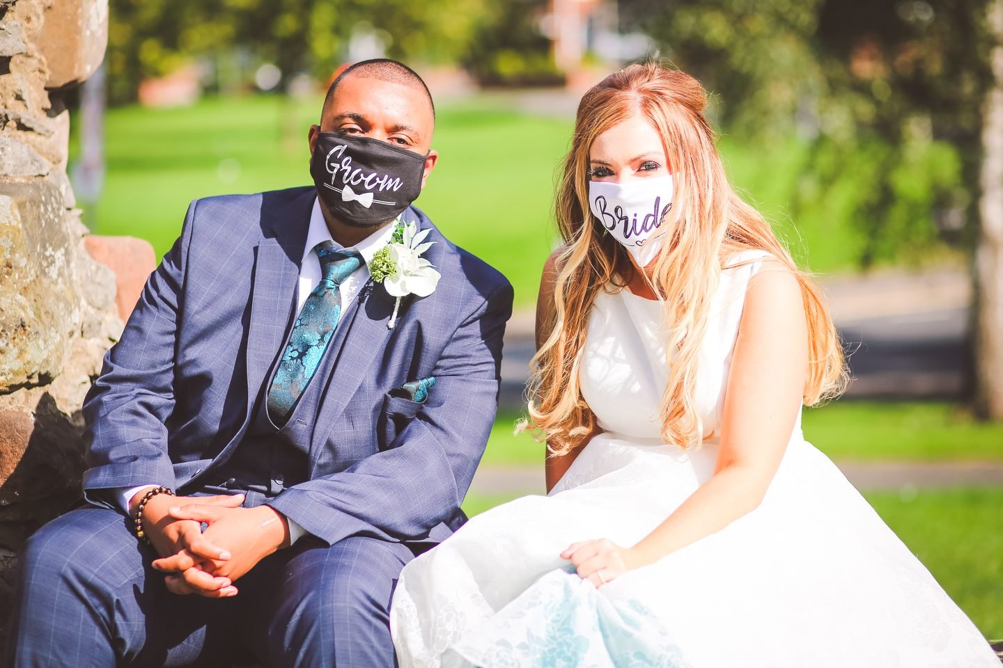 Bride and groom seated outdoors wearing face masks printed with Groom and Bride