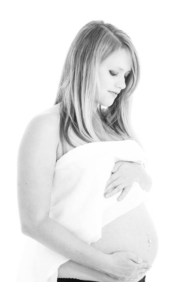 High key black and white maternity portrait of a woman cradling her bump