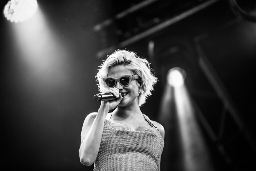 Black and white live portrait of Pixie Lott smiling in sunglasses as she sings