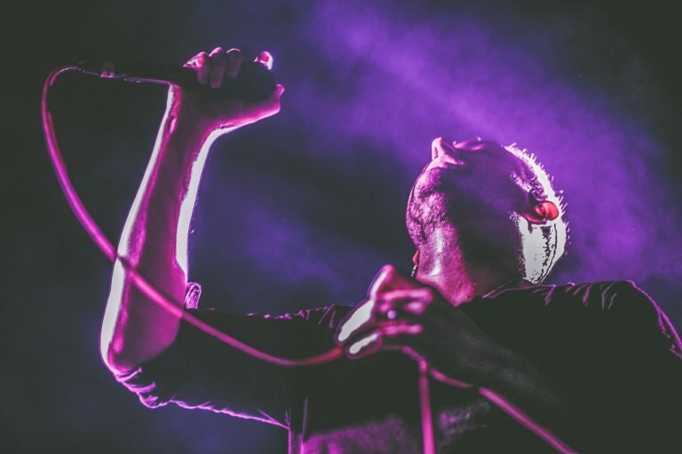 Close-up of a Mogwai vocalist gripping a microphone and cable under purple and pink light
