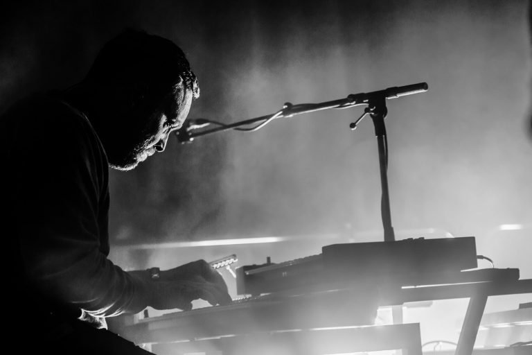 Black and white photograph of a keyboard player in silhouette surrounded by stage haze