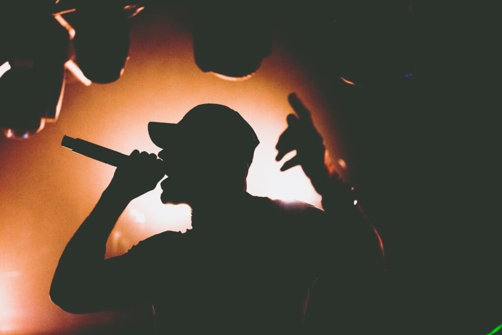 Silhouette of a rapper in a cap holding a microphone against warm orange backlight