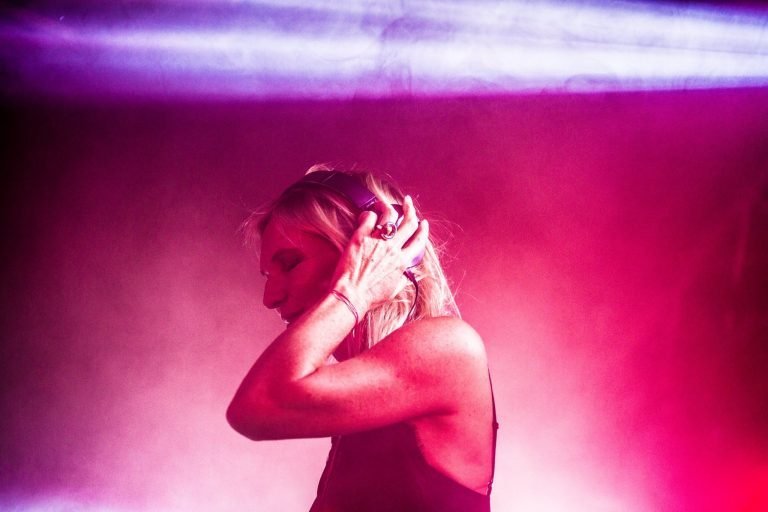 Jo Whiley DJing in headphones under pink and red light at a 90s anthems night in Birmingham