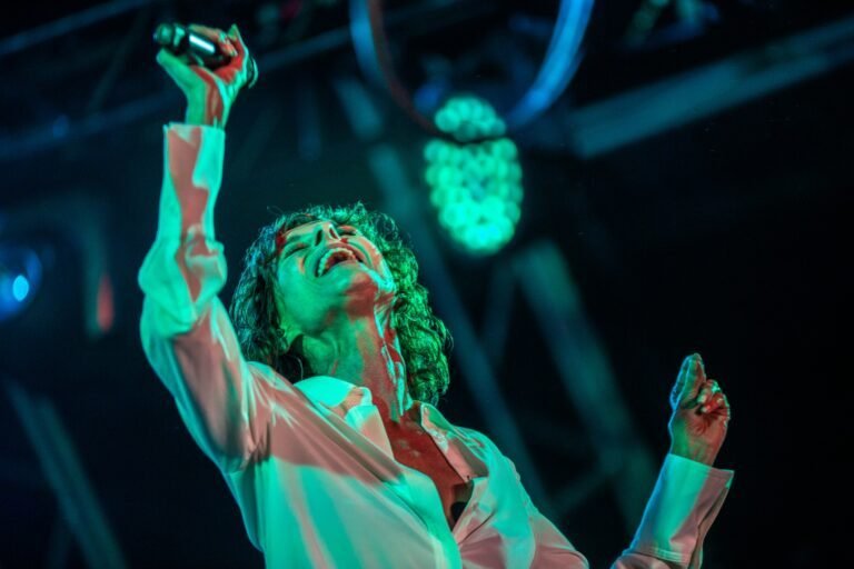 Lisa Stansfield singing with arms raised under green stage lighting