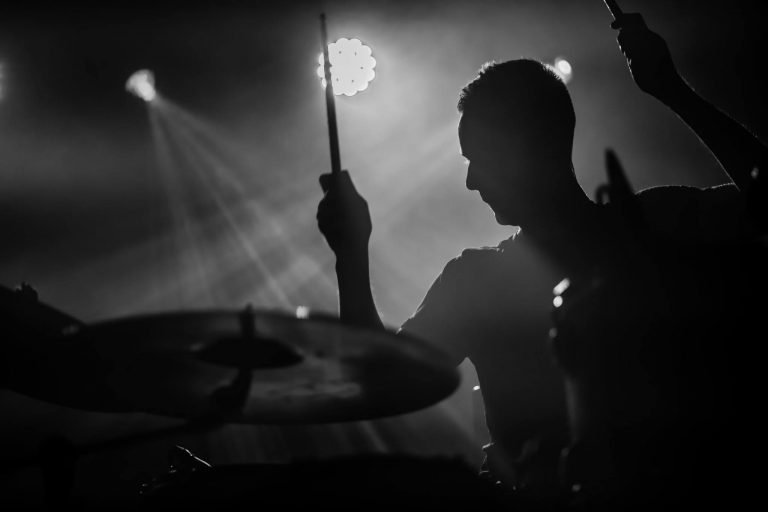 Black and white silhouette of a Mogwai drummer, stick raised, against stage lights