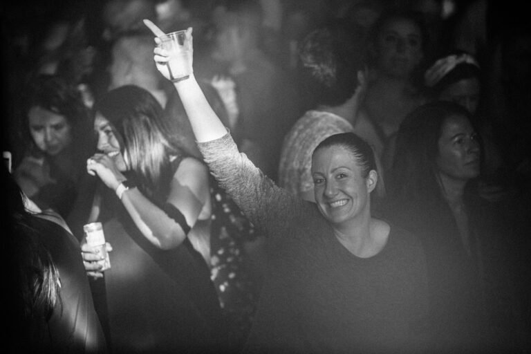 Black and white photograph of smiling women in a hazy crowd at a 90s anthems night