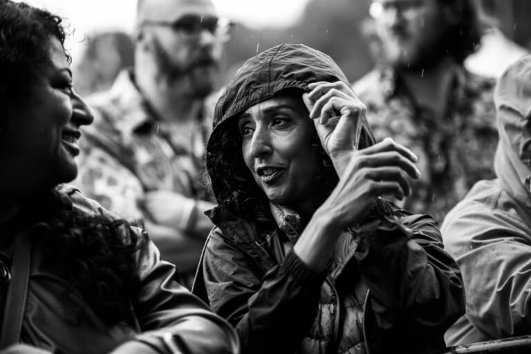 Black and white photograph of festival goers in hooded jackets chatting in the rain at Solihull Summerfest