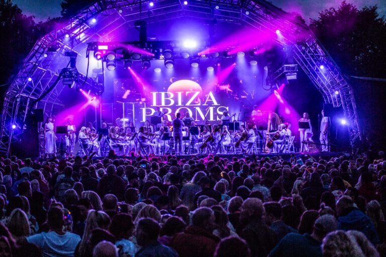 The Ibiza Proms orchestra on a stage lit purple and pink above a large crowd in Solihull