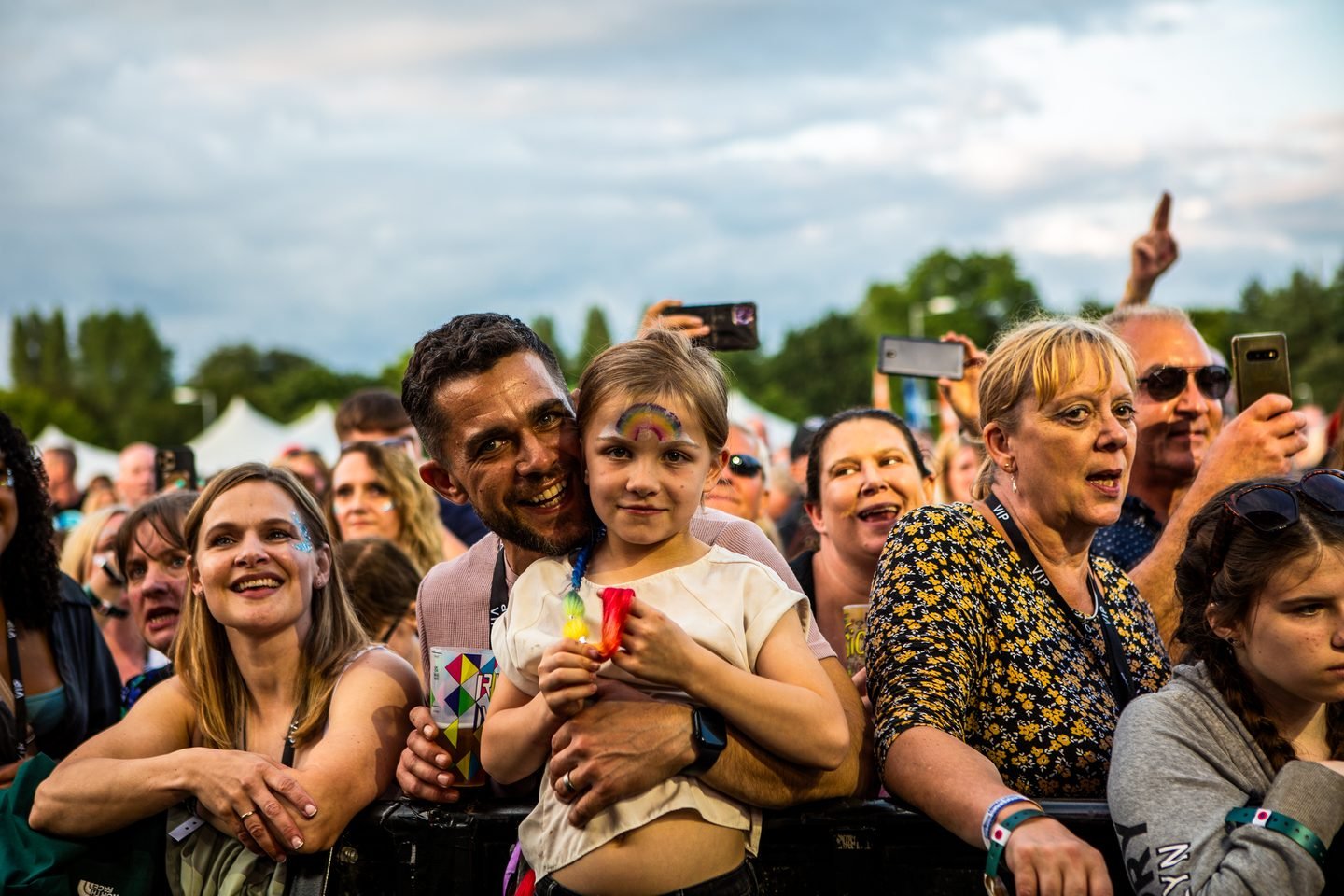 A father holding his face-painted daughter at the front of the crowd at Solihull Summerfest