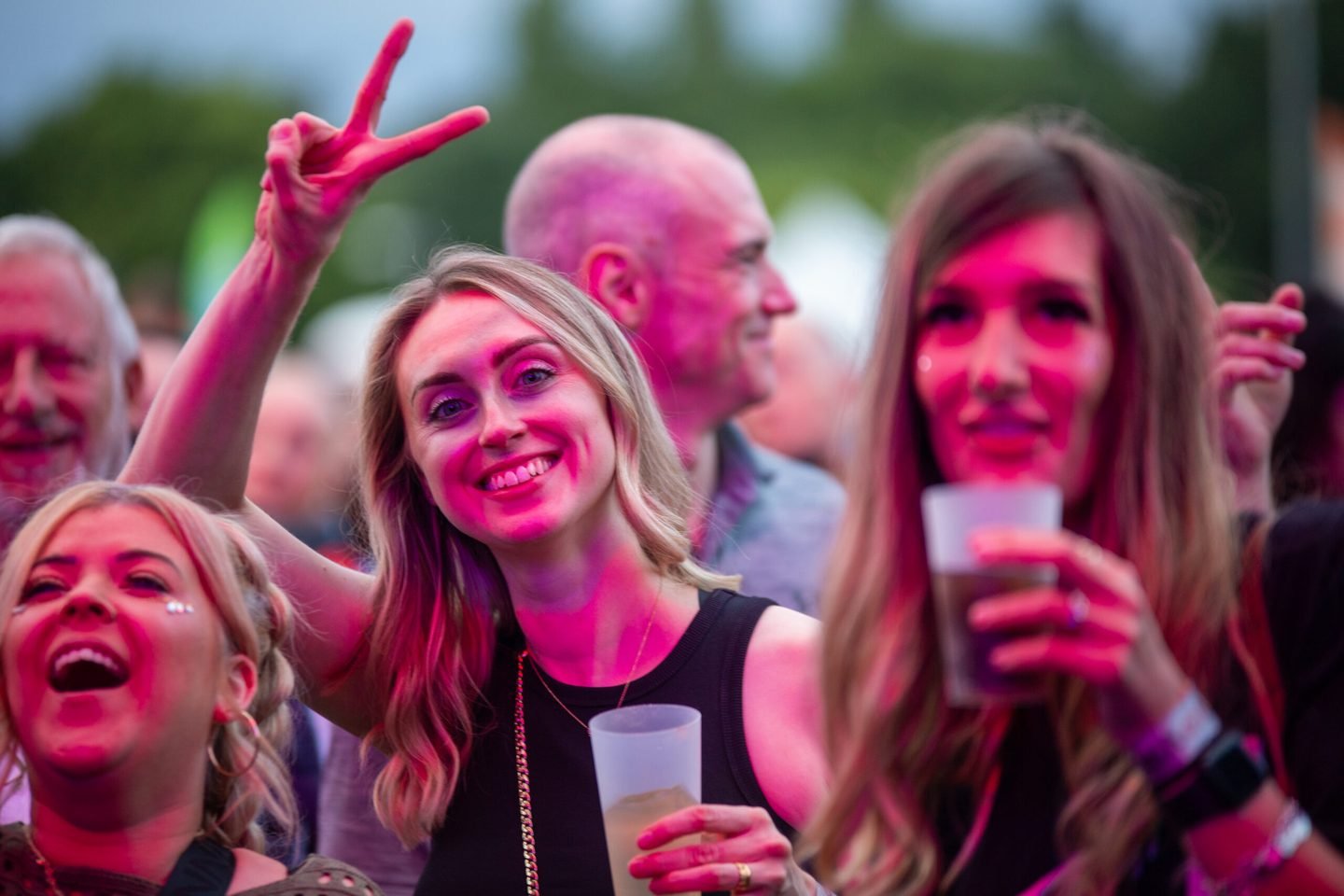 Friends smiling and making peace signs in the crowd under pink light at Ibiza Proms, Solihull