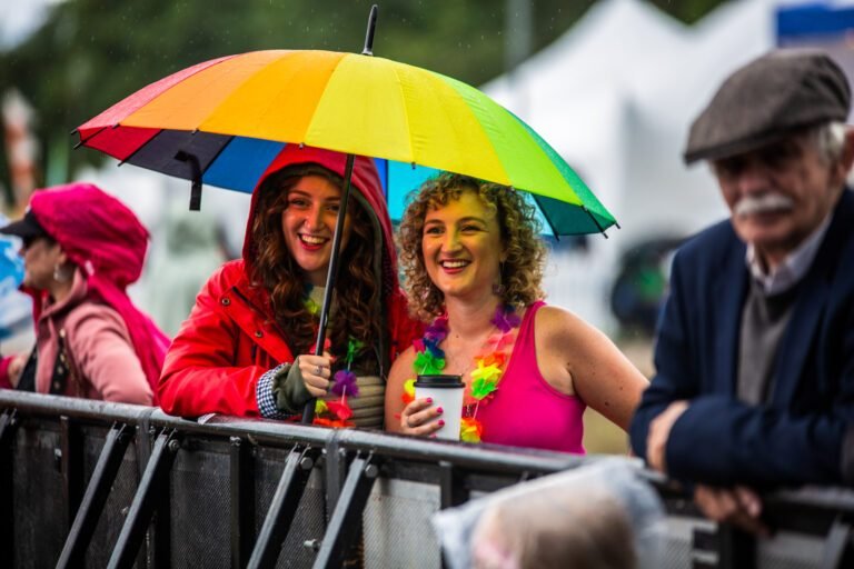 Two women laughing under a rainbow umbrella at the barrier at Solihull Summerfest