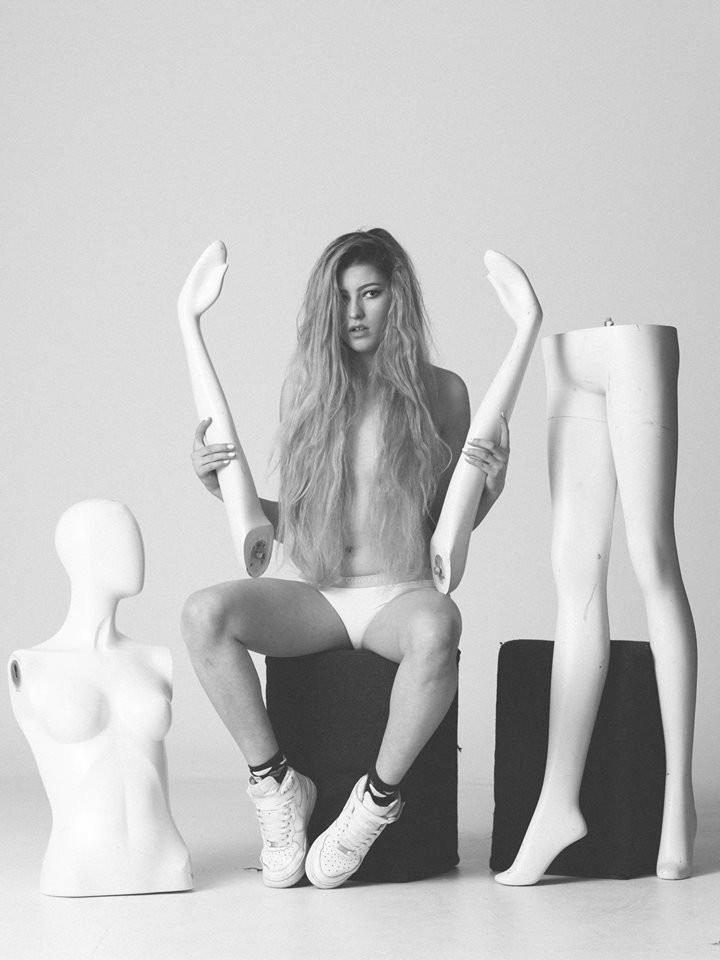Black and white conceptual studio portrait of a model seated among mannequin parts