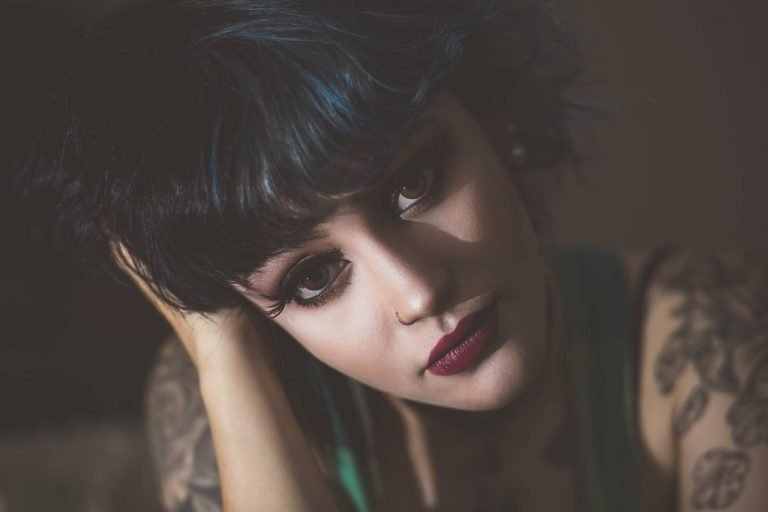 Moody close-up portrait of a woman with dark hair and tattoos resting her head on her hand