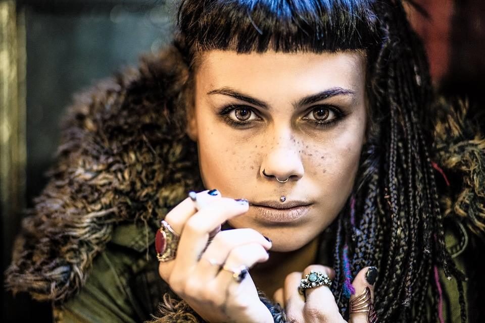 Close-up colour portrait of a woman with braids, freckles and rings, in a fur-trimmed coat