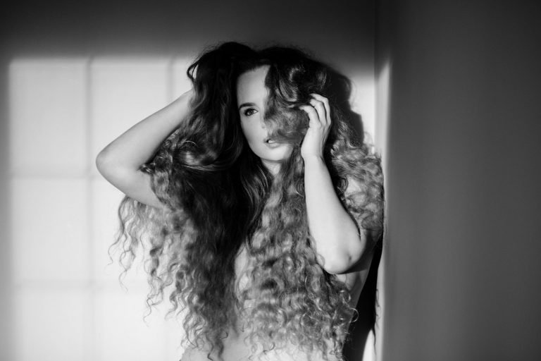 Black and white portrait of a woman with long curly hair beside a window