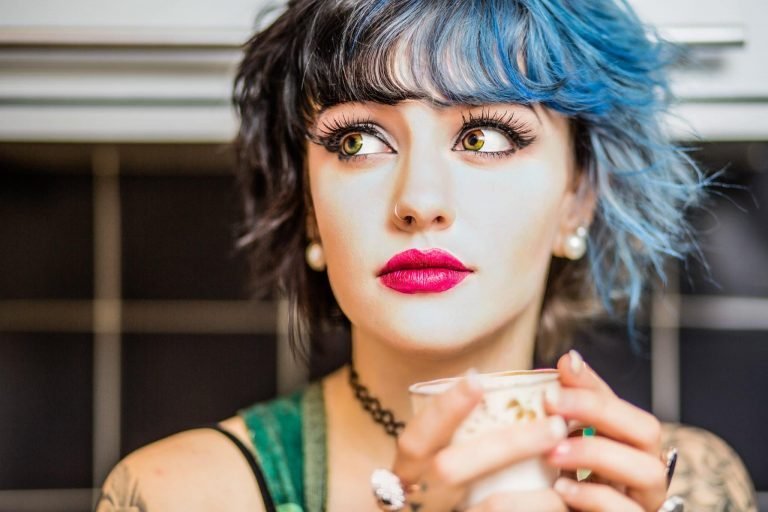Portrait of a woman with a blue fringe and pink lipstick holding a teacup