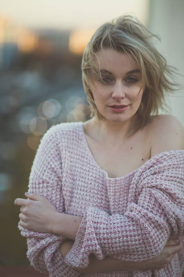 A woman in a pink knitted jumper at golden hour with soft bokeh behind her