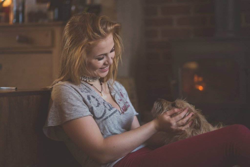 A laughing woman stroking her dog in warm light at home