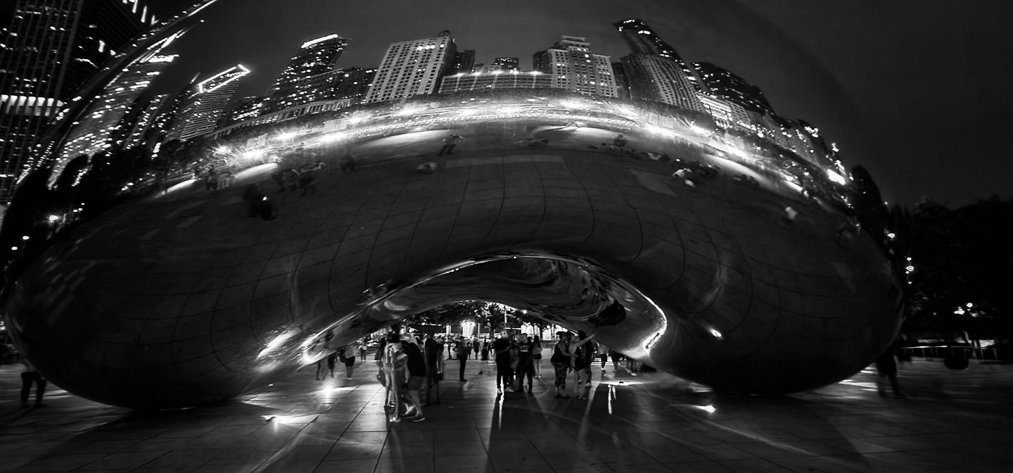 Black and white photograph of Cloud Gate in Chicago at night reflecting the city skyline