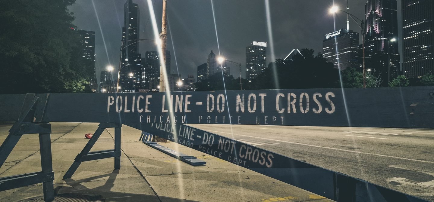 Police line tape strung across a Chicago street at night with skyscrapers behind
