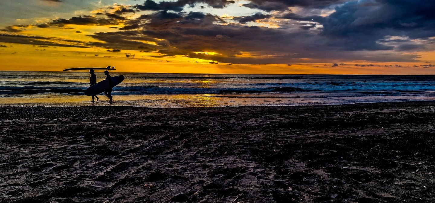 Surfers carrying boards in silhouette along a Costa Rica beach at sunset