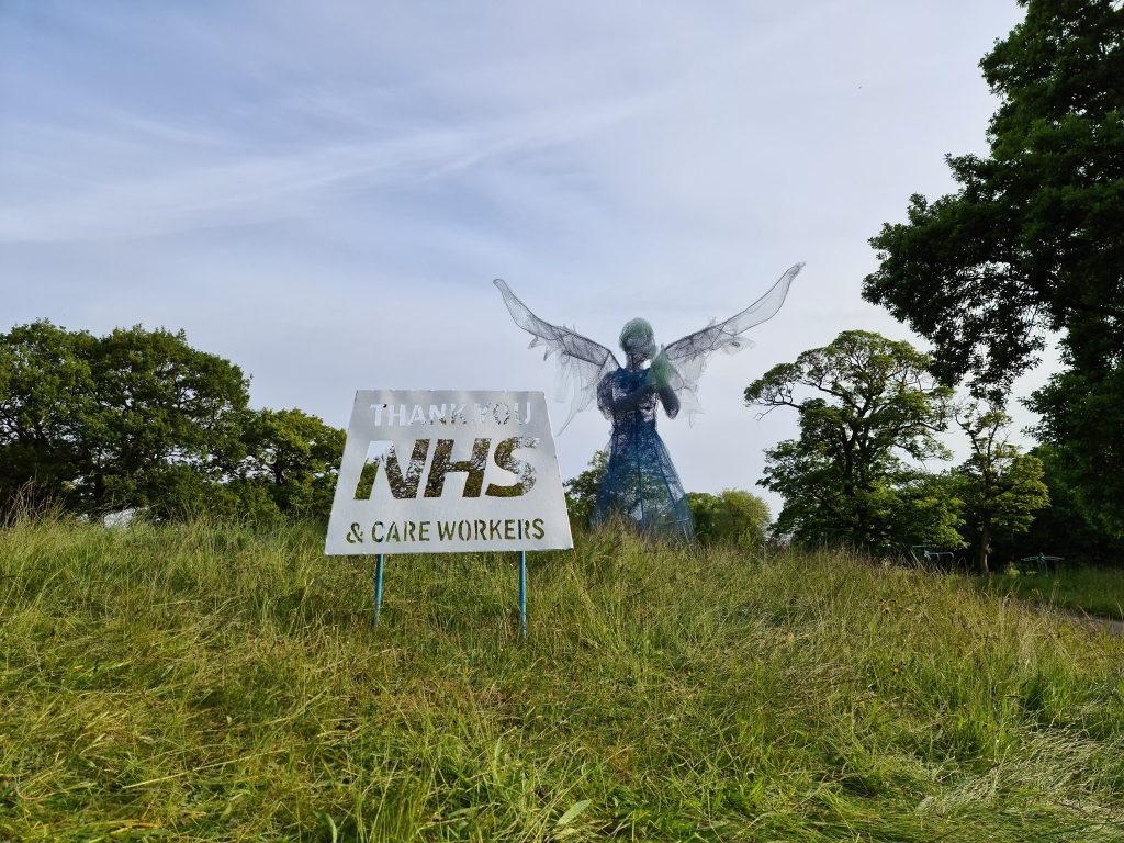A winged angel sculpture behind a Thank You NHS and Care Workers sign, Birmingham lockdown 2020