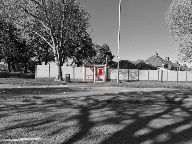 Tree shadows across an empty road by a red bus shelter, Birmingham lockdown 2020