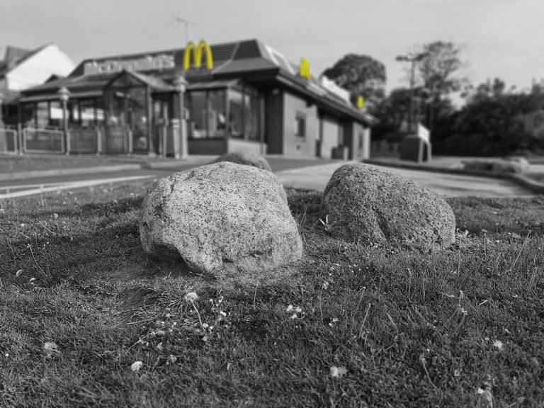 Black and white photograph of boulders on the grass outside a closed McDonald's, Birmingham lockdown 2020