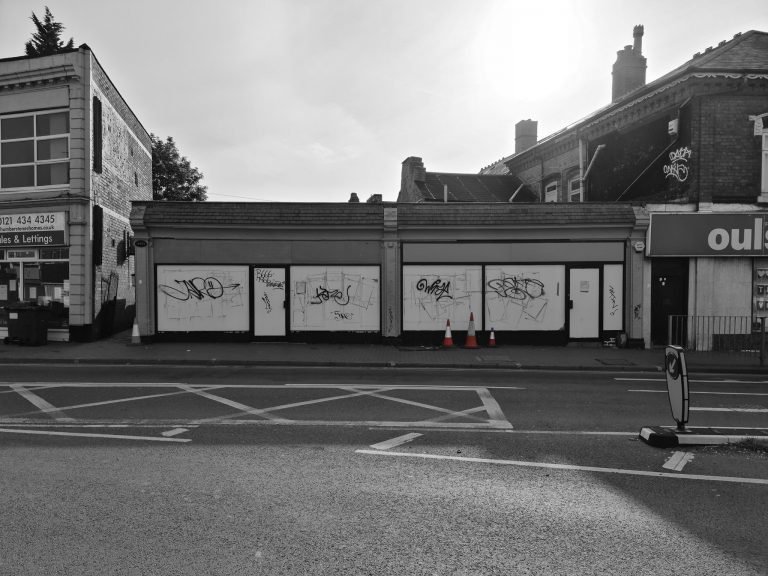 Black and white photograph of graffiti-covered shutters on a closed parade, Birmingham lockdown 2020