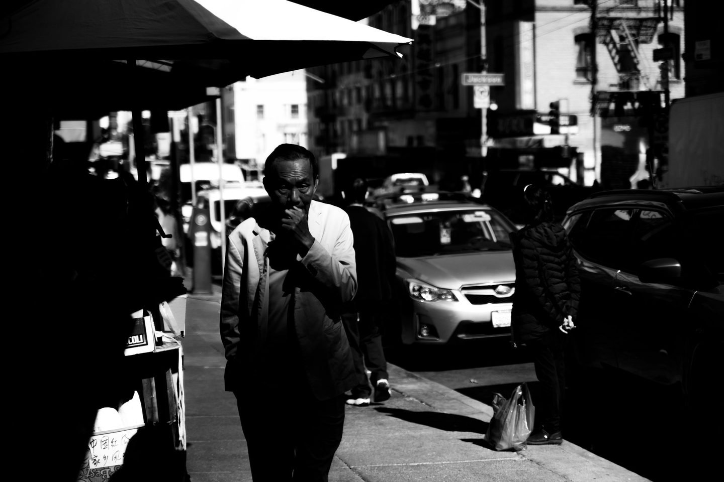 Black and white street portrait of a man smoking on a Chinatown pavement in San Francisco