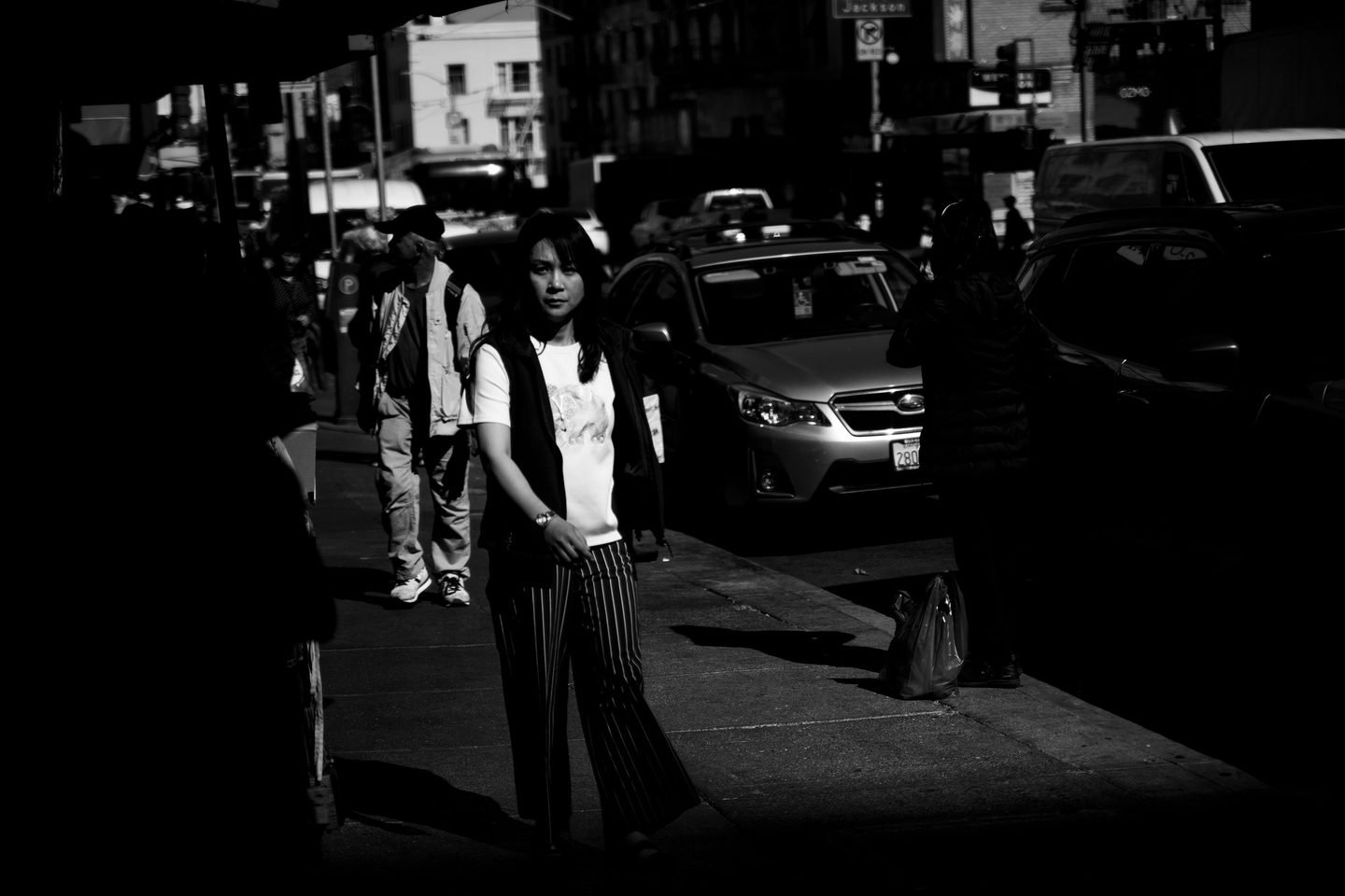 Black and white street photograph of a woman stepping into hard light in Chinatown, San Francisco