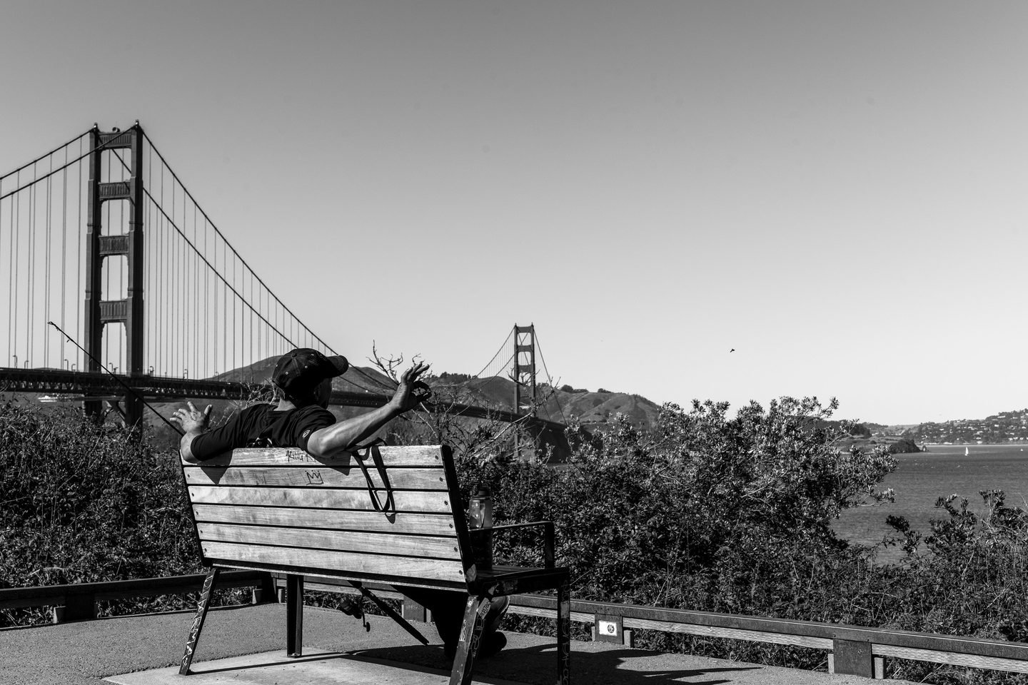 Black and white photograph of a man stretching on a bench overlooking the Golden Gate Bridge